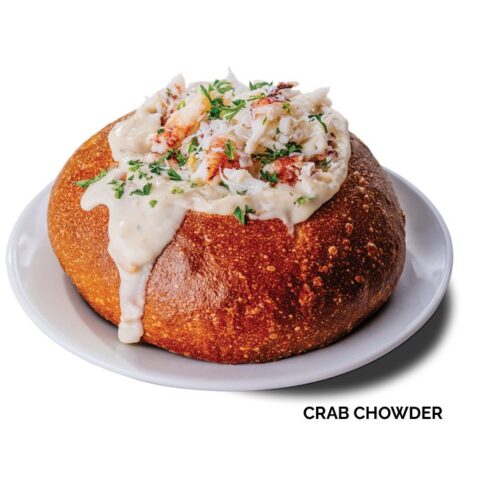 Crab chowder in a sourdough breadbowl topped with crab on a white backdrop