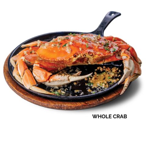 Whole roasted crab on a skillet and topped with garlic sauce