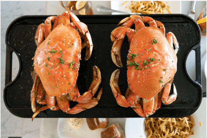 Two San Francisco Dungeness crabs facing each other on a skillet